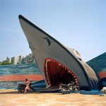 A woman runs while a shark sculpture appears to attempt to devour her