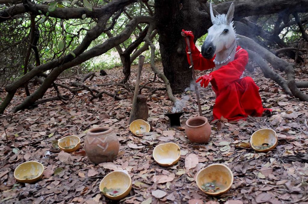 a ritual being conducted in the woods by a horse-headed figure in red robes