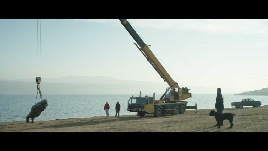 a crane lifting a statue on the beach
