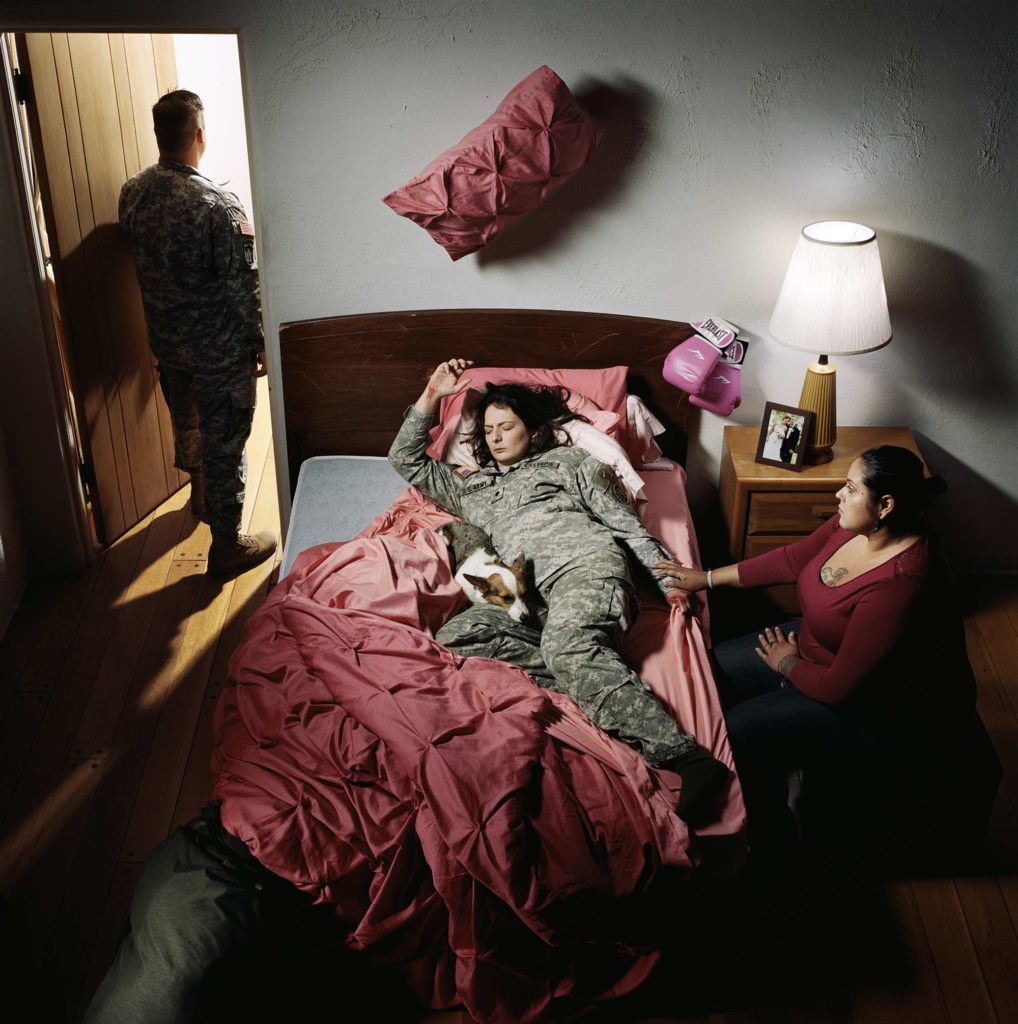 a woman soldier on a bed with someone watching over her as she sleeps
