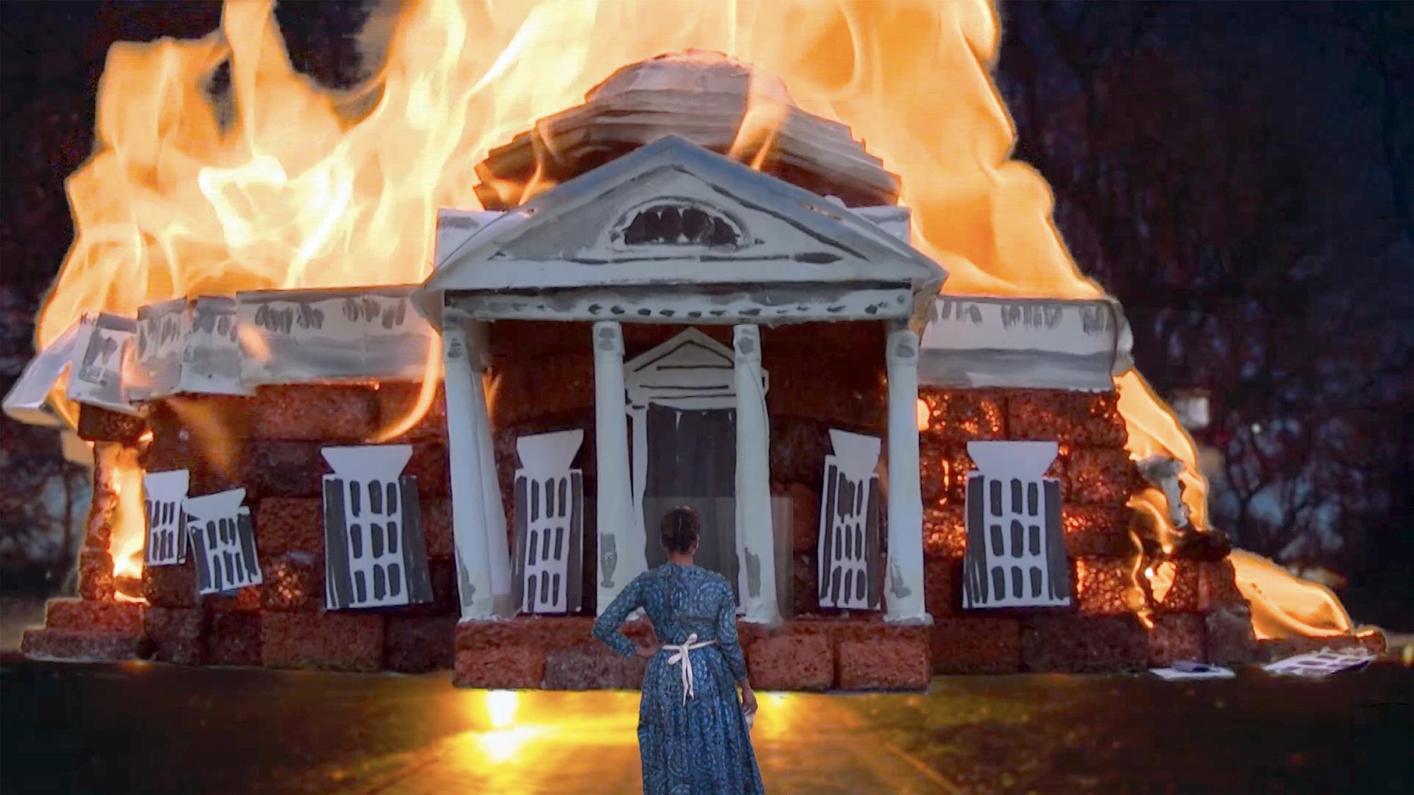 a woman in traditional clothes stands before a burning building
