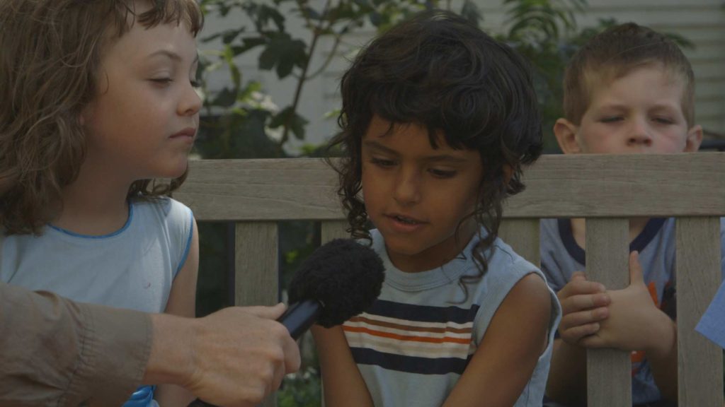a child ponders with a microphone in front of her as other children watch
