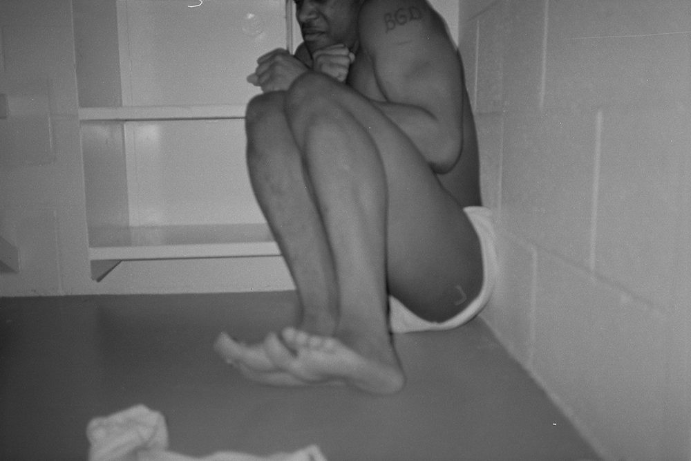 A prisoner curled up in a defensive posture in the corner of their cell.