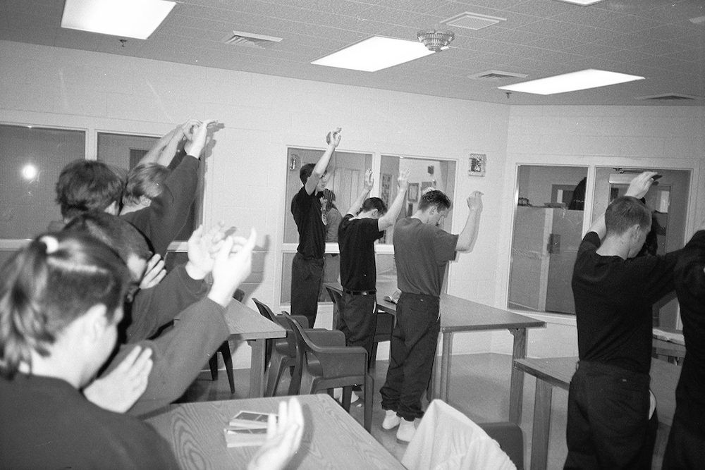 Prisoners standing with hands up in the air, facing away from the camera.