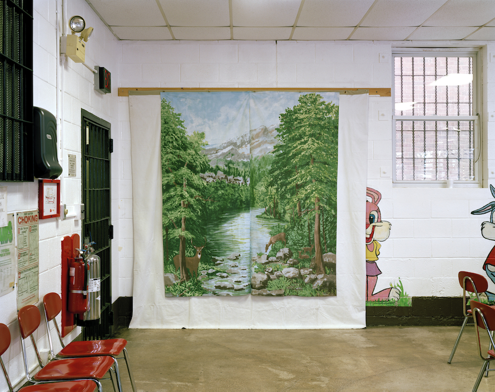 A backdrop of a forest hangs on a wall where photos are taken within Woodbourne Correctional Facility