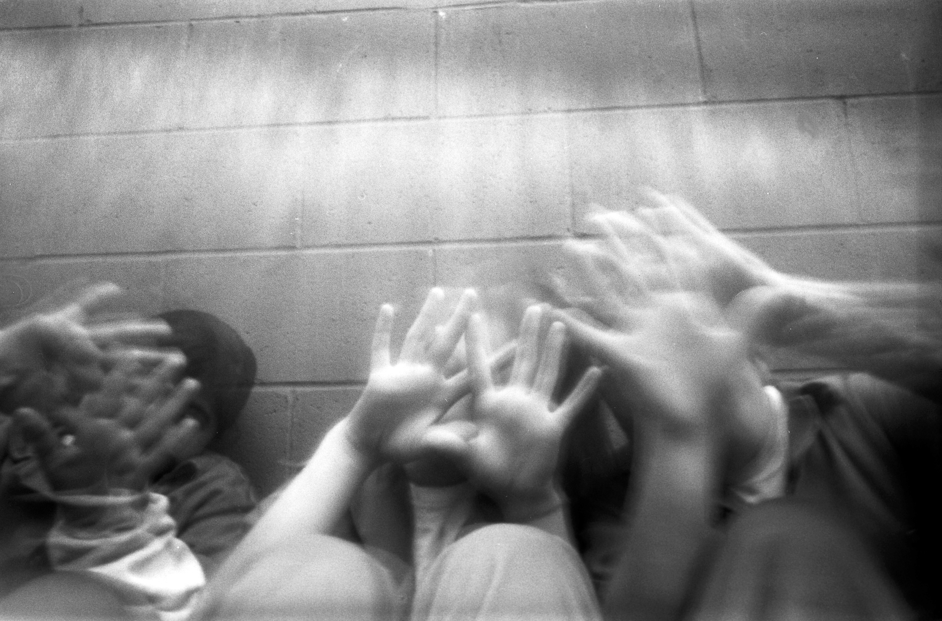 Black & white photo of girls holding hands up, obscuring their faces.