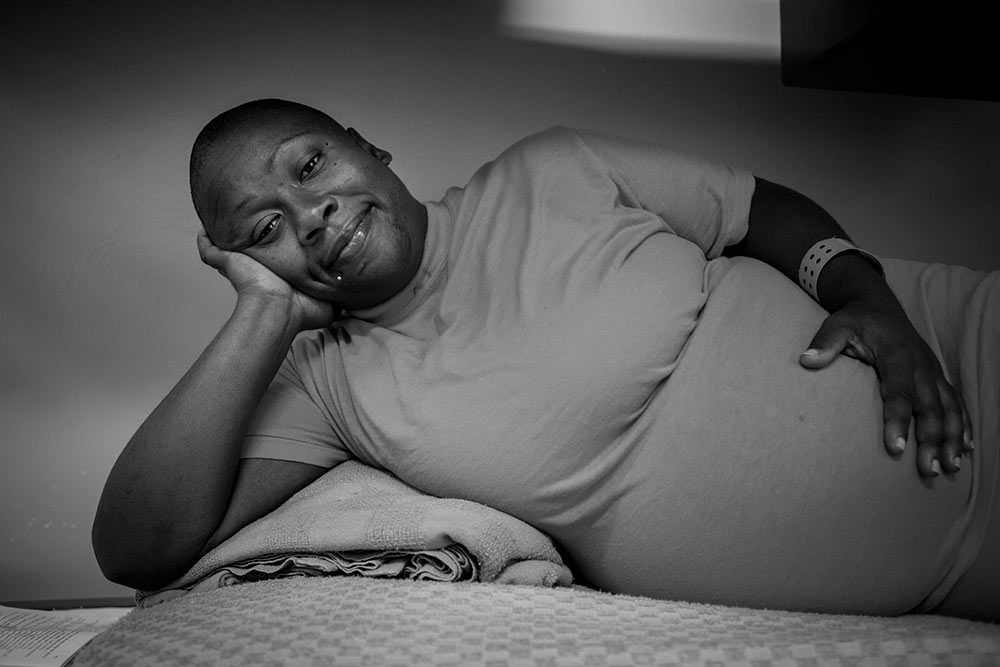 A pregnant female prisoner lying in her bunk, smiling at the camera.