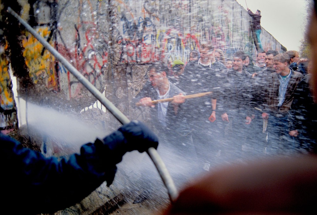 Alexandra Avakian Young West German Men Attack the Berlin Wall while East German Guards Shoot Water Cannon through the Cracks, 1989 Collection of the Artist